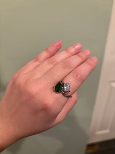Reviewer's hand wearing the Navae Birthstone Ring with a green pear-cut and a clear radiant-cut stone.