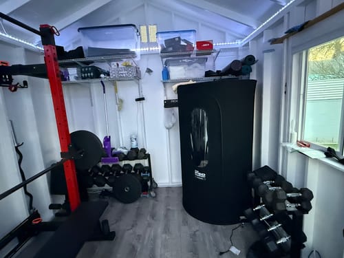 Customer's fully assembled black Sauna Pod 2.0 set up in a home gym next to exercise equipment.