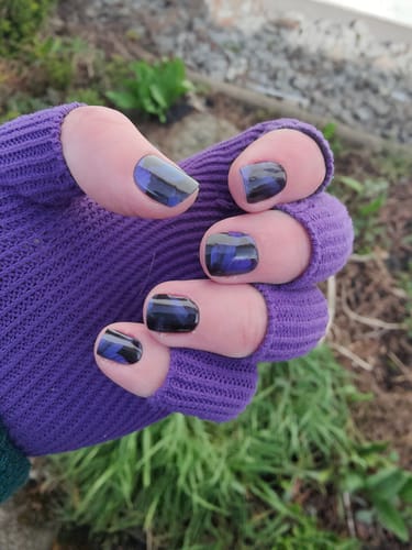 Die Hand eines Kunden in einem lila Handschuh, der die „Twilight Woods“ UV-Gel-Nagelfolien mit lila-schwarzem Muster zeigt.