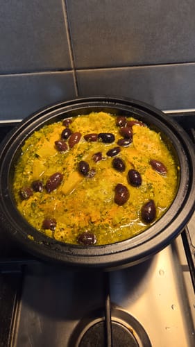 Recensent toont een gerecht met olijven in de Le Creuset Tajine op een kookplaat.