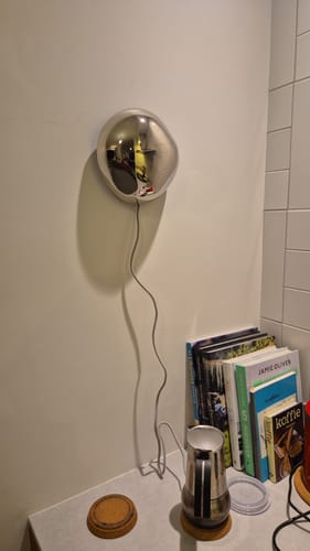 Een recensent toont de glanzende, chromen Orb wandlamp gemonteerd aan een witte muur.