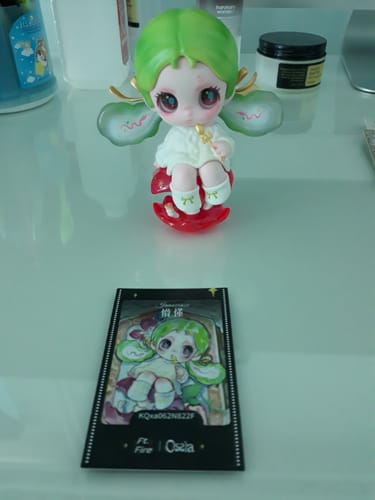Customer's Ossia 'Innocence' figure with green hair and a white outfit, sitting on a translucent red apple base with its card.