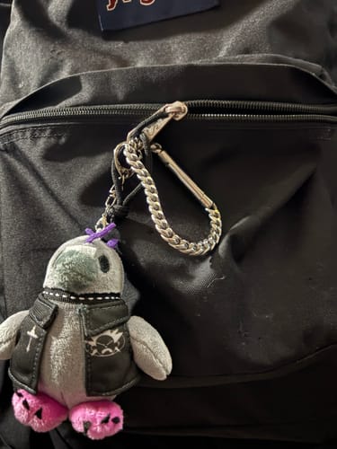 Customer's Phoenix The Punk Pigeon mini plushie keychain clipped to the zipper of a black backpack.