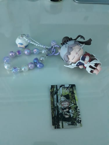 Reviewer's handmade keychain with a cute sleeping figure and a purple beaded strap, displayed next to its character card.