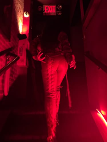 Reviewer from behind wearing the tan Vice Pant while walking up a dark, red-lit staircase.