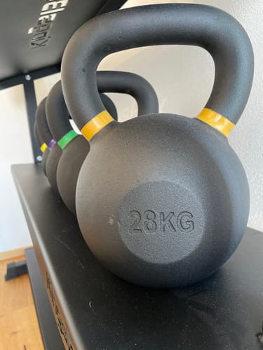 Customer's set of black kettlebells on a rack, highlighting the 28 KG weight with its yellow-banded handle.