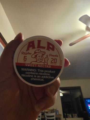 A customer's hand holding a round, white tin of ALP Sweet Nectar Nicotine Pouches.