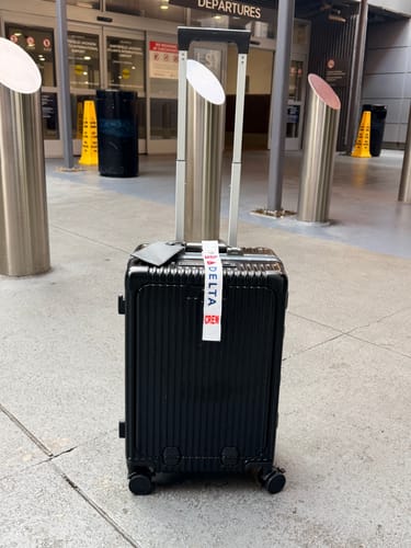 Customer's black All-in-One Carry-On with an extended handle standing in an airport departure area.