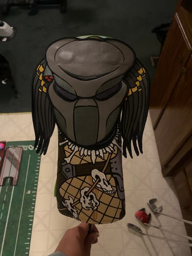 A reviewer displays their Predator "Jungle Hunter" Driver Headcover, featuring the character's detailed bio-mask.