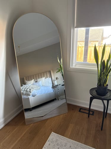 Customer's Gold Full Length Arch Mirror leaning in the corner of a bedroom next to a window.