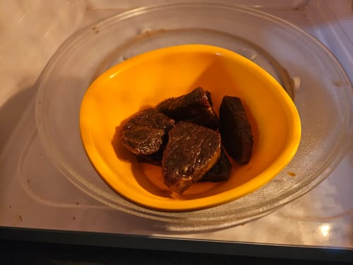 Cliente mostrando su Cecina de Res Original en un tazón amarillo dentro del microondas.