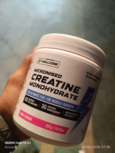 Customer holding a white tub of Wellcore Pure Micronised Creatine Monohydrate in the Fruit Fusion flavor.