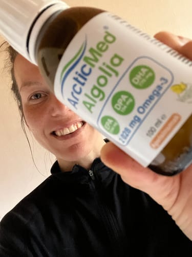 En leende recensent som håller i en flaska ArcticMed Algolja framför kameran.