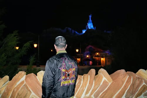 Customer from behind wearing the black Powerline coach jacket at a theme park at night.