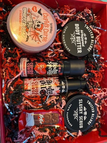 Customer's Cupids Curse Set arranged in a red box with decorative paper, showing the body oil, spray, scrub, and soap.