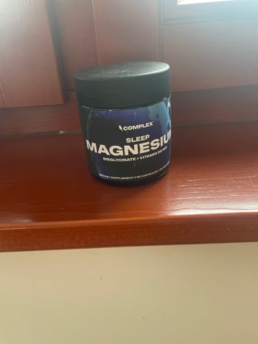 A customer's black jar of Complex Sleep Magnesium supplement resting on a wooden surface by a window.