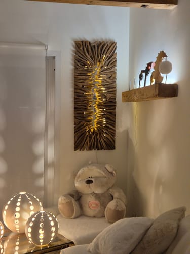 Kundenfoto der leuchtenden LUMINA LED-Treibholz-Wandlampe, die an der Wand über einem Teddybären hängt.