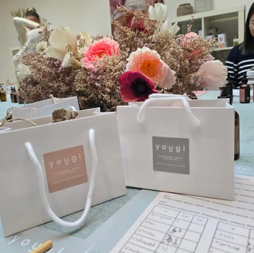 Reviewer's view of the Perfume Making Workshop, with branded take-home bags and a scent creation sheet on the table.