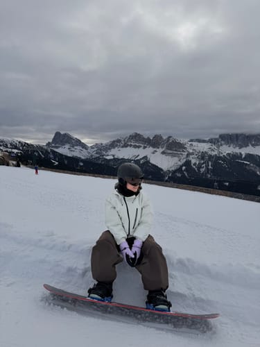 Reviewer sitting on a snowboard while wearing the off-white snow jacket on a snowy mountain.