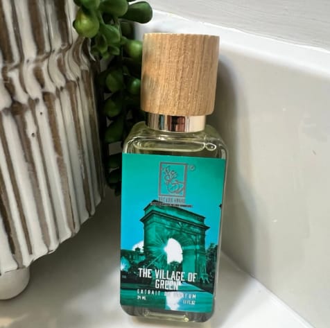 Customer's bottle of The Village Of Green perfume with a turquoise label and wooden cap on a bathroom counter.