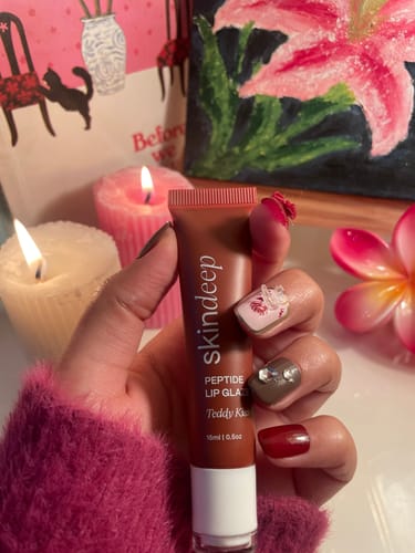 Customer holding the Peptide Lip Glaze tube in a softly lit room with candles.