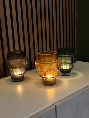 Recensent toont drie gekleurde POLSPOTTEN Steps waxinelichthouders, die sfeervol branden op een dressoir.