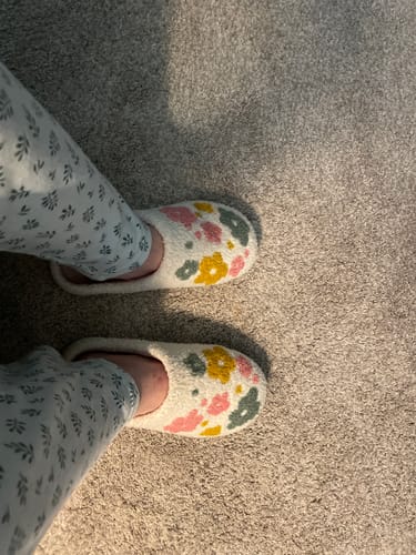 A reviewer wearing the plush, floral-patterned Lover's Plush Slippers indoors on a carpeted floor.