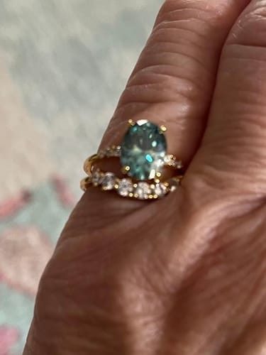 Customer's hand wearing the two-band Serapha ring, showing the oval green-blue stone and gold setting.