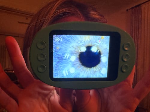 Ein Kunde demonstriert die starke Vergrößerung des grünen Geräts mit einer Nahaufnahme seines Auges.