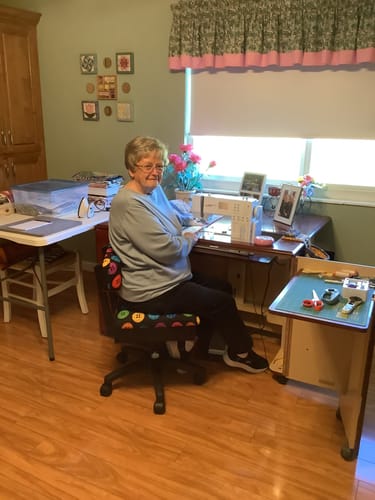 Reviewer sitting on the patterned Arrow Hydraulic Sewing Chair while working at a sewing machine.