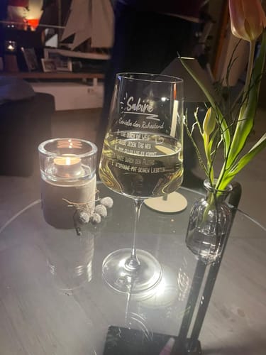 Ein Kunde zeigt das gravierte Leonardo Weinglas für 'Sabine' mit Weißwein bei Kerzenlicht auf einem Tisch.