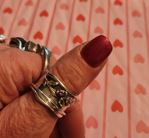 Close-up of a customer's hand wearing the Rose Flower Fidget Ring with green and purple gemstones.