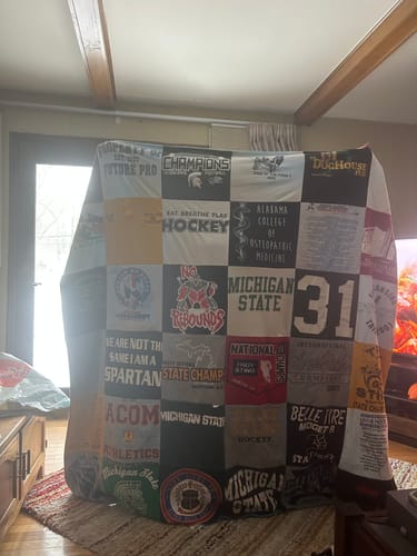Customer's large Premium T Shirt Quilt made from sports and school shirts, standing upright in a living room.
