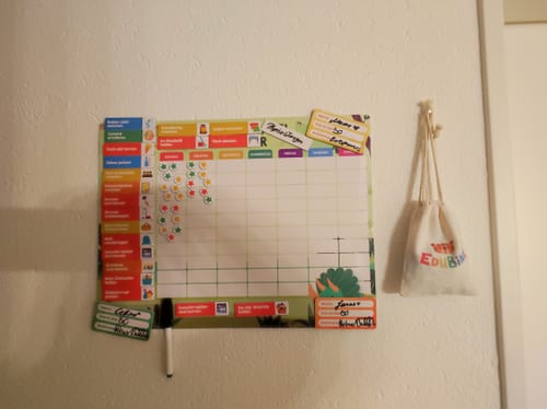 Rezensent zeigt die Edubini Belohnungstafel® in Gebrauch an einer Wand, bereits mit vielen Sternen gefüllt.