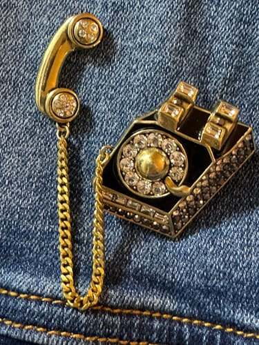 Reviewer's black and gold crystal "Gossip Girl" telephone pin shown on a blue denim jacket.