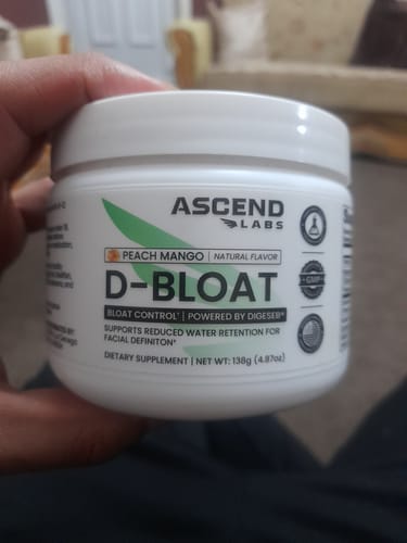 Reviewer holding a white tub of D-BLOAT dietary supplement in Peach Mango flavor.