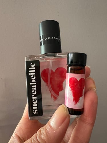 Reviewer's hand holding the full-size bottle and a small sample vial of Love Dust perfume.