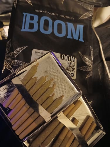 Customer's silver case filled with rolled cones of Bubba Kush Smalls, with the product's black packaging in the background.