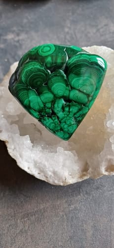 Client montrant une pierre de Malachite polie et verte, posée dans une géode de quartz.