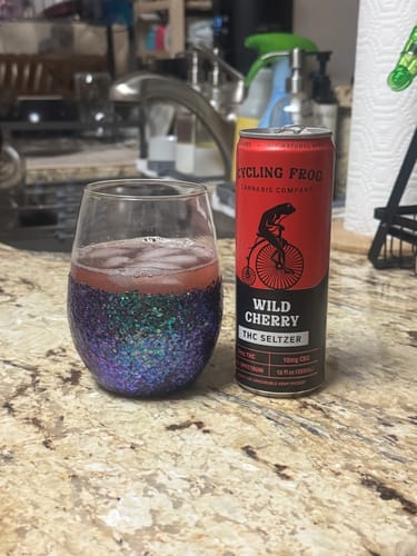 Reviewer's can of Wild Cherry THC Seltzer next to a sparkly glass of the beverage poured over ice on a counter.
