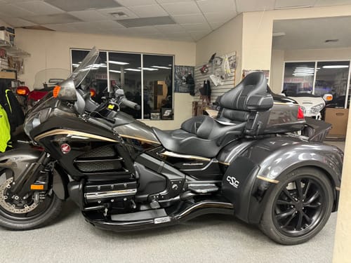 Reviewer's shiny, dark three-wheeled motorcycle parked in a showroom, highlighting the product's high-shine finish.