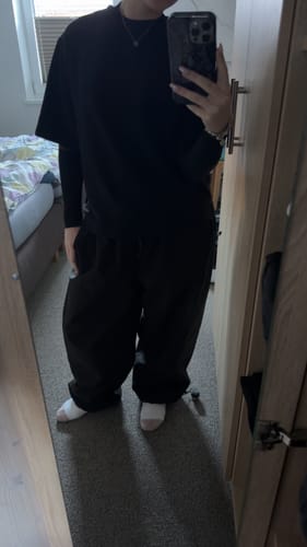 Reviewer wearing the baggy black snow pants indoors, showing the oversized fit from a mirror selfie.