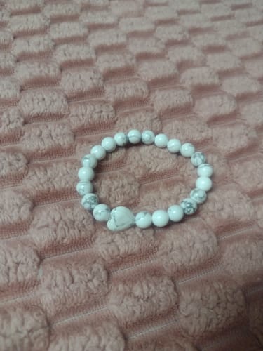 Reviewer's pretty Howlite crystal bracelet with a heart bead on a pink textured surface.