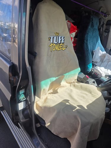 Customer's beige Tuff Towel seat cover draped over a car's driver seat, viewed from the open door.