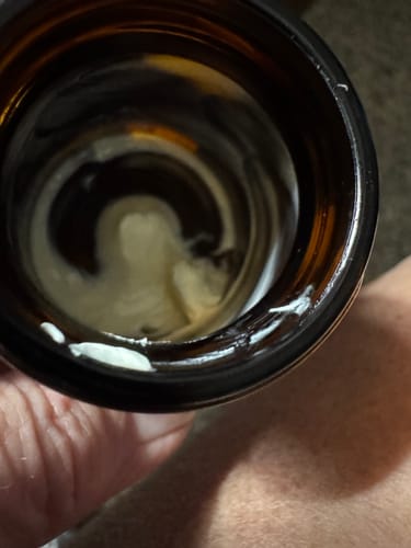 Reviewer holding a nearly empty brown glass jar of CBD + CBN Magnesium Sleep Cream.