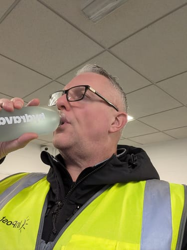 Reviewer in a high-vis vest drinking from the Frosted Hydrava Bottle indoors.
