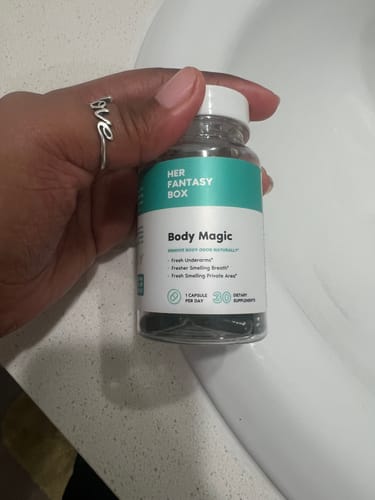 Customer's hand holding a clear bottle of Body Magic Chlorophyll Pills, showing the dark capsules inside.