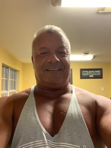 A muscular reviewer in a grey tank top smiling after a workout.