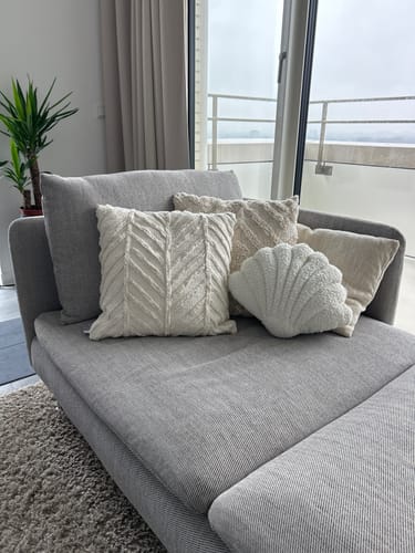 Klant toont het witte, getextureerde sierkussen JULIE op een grijze chaise longue.