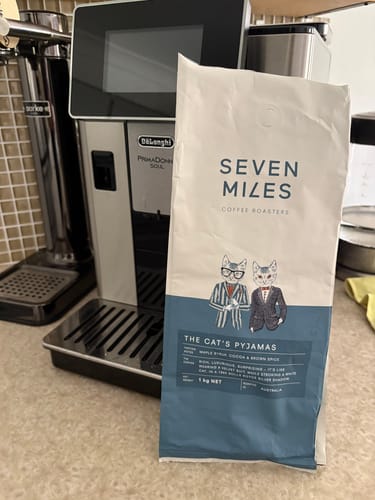 Customer's bag of whole bean coffee on a kitchen counter next to an automatic coffee machine.